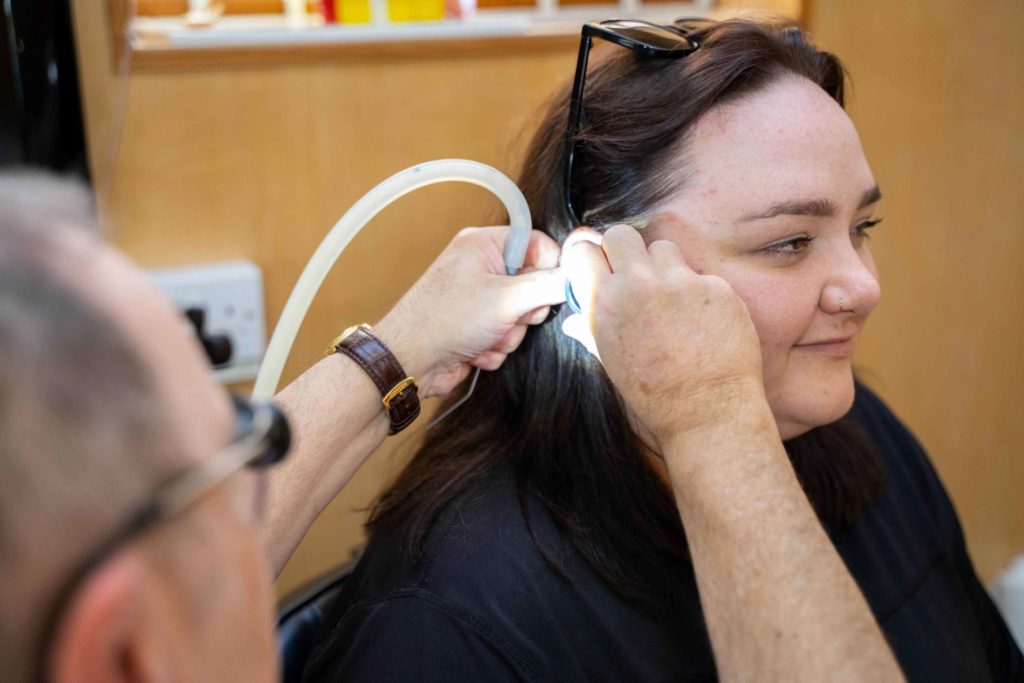 Professional audiologist performing microsuction ear wax removal on a client
