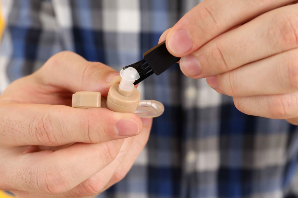 person cleaning a hearing aid using multi-functional tool